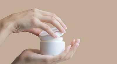 Hands holding and opening a white jar of cream.